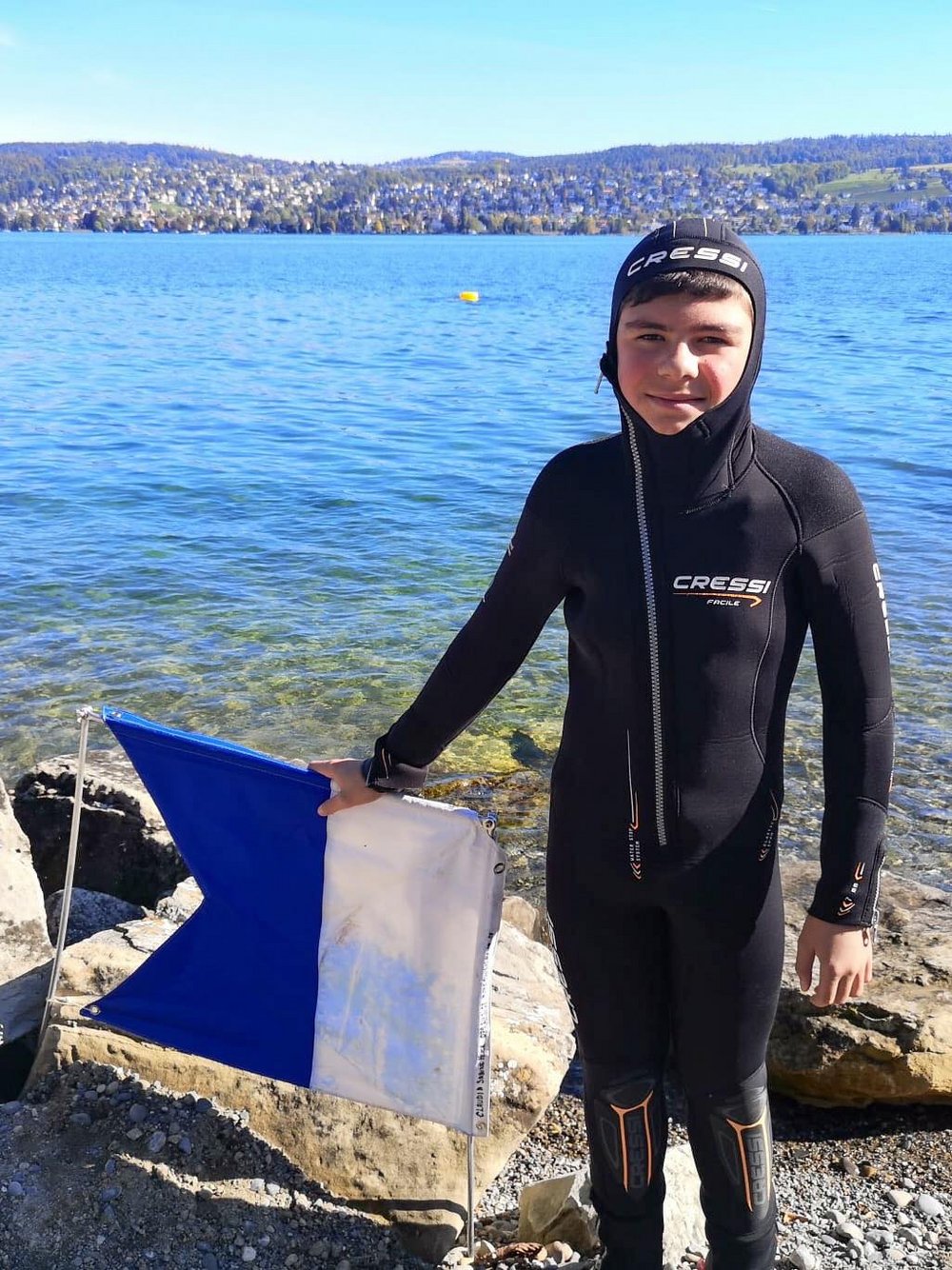 Junior Taucher steht neben Tauchflagge am Seeufer